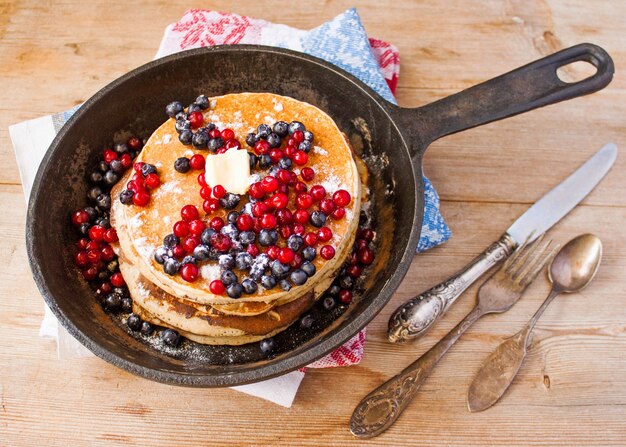 Panquecas fritas caseiras em uma frigideira de ferro fundido preto com frutas vermelhas, framboesas, cranberries e blackberries