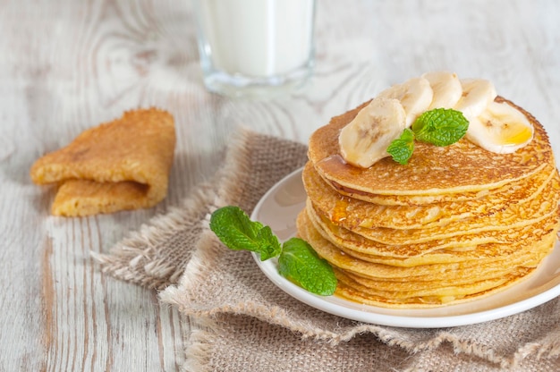 Panquecas servidas com leite guarnecidas com folhas de hortelã e rodelas de bananax