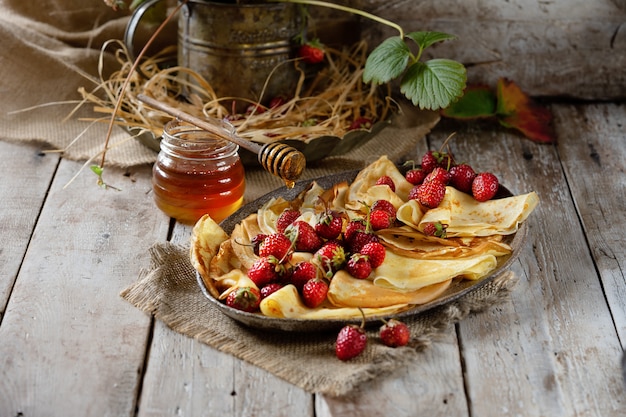 Panquecas tradicionais ucranianas ou russas com morangos e mel na mesa de madeira