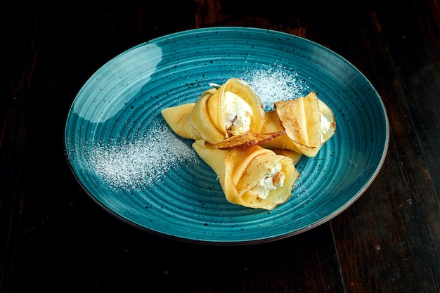 Panquecas ucranianas tradicionais com queijo cottage, servidas em um prato azul com tomate e creme de leite em um fundo escuro.