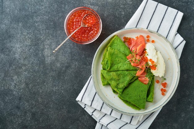 Panquecas verdes Panquecas de crepe de espinafre verdes finas e redondas com caviar vermelho e preto e molho de iogurte em fundo de concreto cinza escuro Café da manhã vegano saudável Dia Nacional da Panqueca ou Dia da Terça-feira Gorda