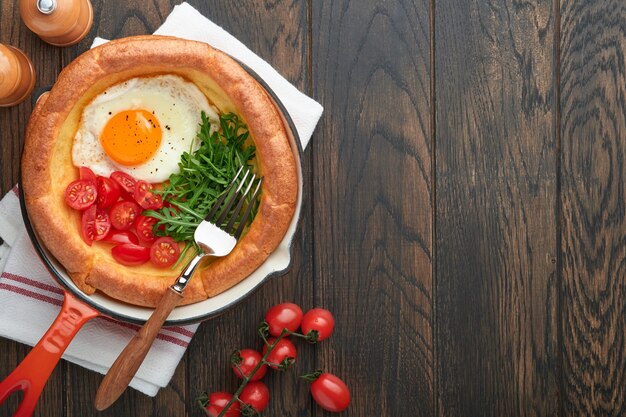 Panqueque de bebé holandés Panqueque de bebé holandés casero fresco con tomate de huevo frito y rúcula verde en una sartén de caña sobre una mesa de madera vieja Plano de cerca