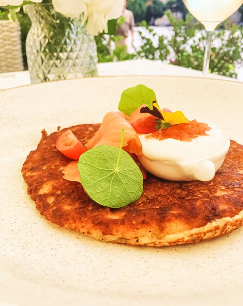 Panqueque de buñuelo de patata con salmón de caviar rojo y crema agria en un restaurante de lujo al aire libre en verano