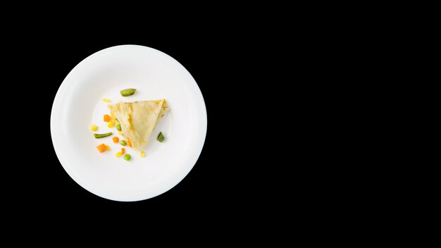 Un panqueque delgado con un relleno saludable en un plato blanco, sobre una pared negra con espacio de copia.