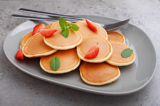 Foto panqueque en un plato con fresas decoradas con menta sobre una mesa de hormigón