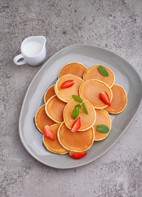 Panqueque en un plato con fresas decoradas con menta sobre una mesa de hormigón