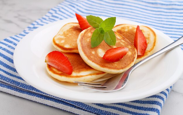 Panqueque en un plato con fresas decoradas con menta sobre una mesa de mármol