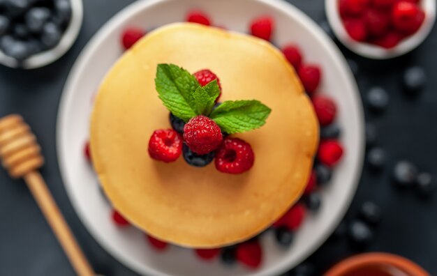 Panqueques americanos con frambuesas, arándanos frescos y miel. Desayuno saludable en concreto