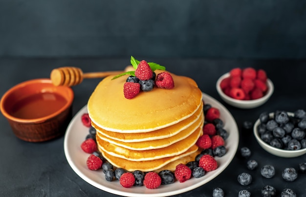 Panqueques americanos con frambuesas, arándanos frescos y miel. Desayuno saludable en concreto