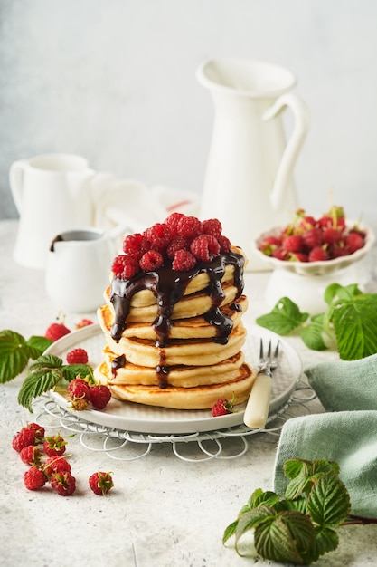 Panqueques americanos Pila de panqueques con frambuesa fresca con glaseado de chocolate o coberturas en un tazón blanco sobre fondo de mesa gris claro Panqueques americanos clásicos caseros Concepto de revista Vista superior