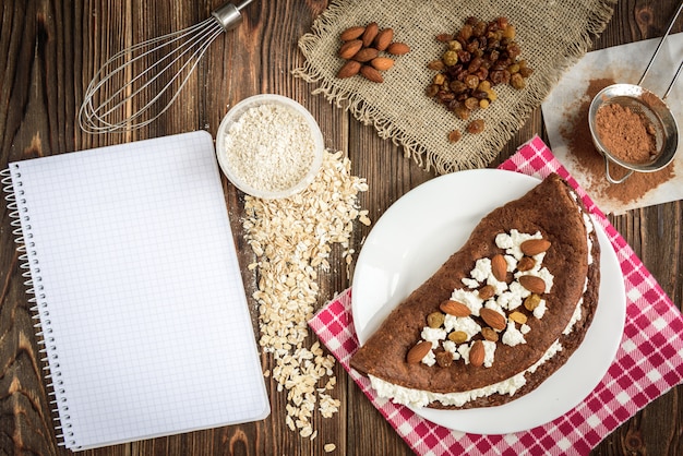 Panqueques de avena con chocolate casero con requesón en plato blanco sobre mesa de madera oscura.