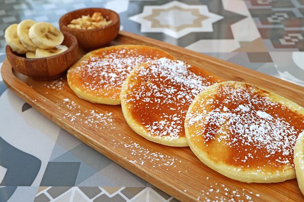 Panqueques con azúcar glas sobre un plato de madera servido en una mesa de piedra estampada