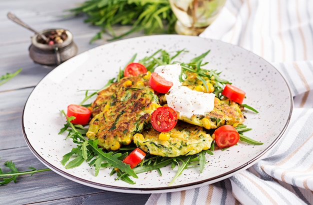 Panqueques de calabacín con maíz y crema agria servidos rúcula, ensalada de tomates.