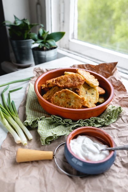 Foto panqueques con calabacín y repollo con aderezo de yogur y hierbas en la mesa junto a la ventana