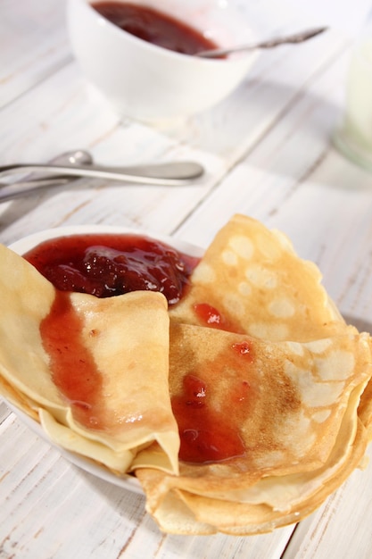 Panqueques calientes finos con mermelada de fresa en una mesa de madera blanca Holiday Maslenitsa