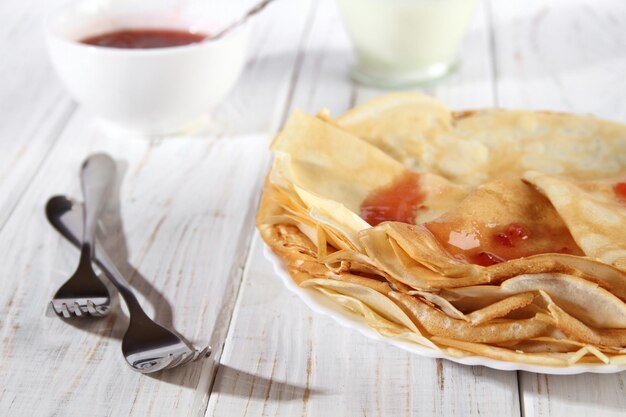 Panqueques calientes finos con mermelada de fresa en una mesa de madera blanca Holiday Maslenitsa