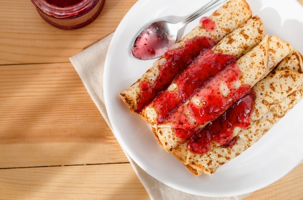 Panqueques calientes en pila en un plato con una cuchara vertida con mermelada