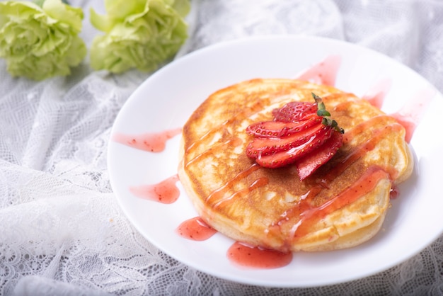 Panqueques caseros con fresas y miel en un plato rosado sobre una superficie de madera blanca