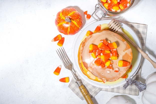 Panqueques caseros de maíz dulce. Pila de panqueques amarillos y naranjas con salsa dulce y dulces tradicionales de Halloween.