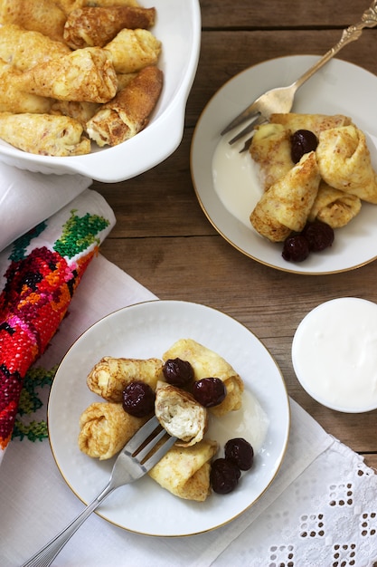 Panqueques caseros rellenos de requesón con pasas, servidos con crema agria y cereza.