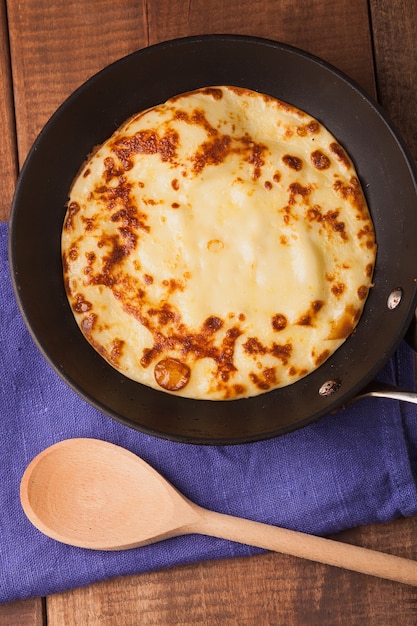 Panqueques caseros en una sartén con crema de cuchara de madera en la mesa de madera