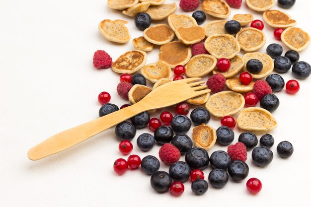 Panqueques de cereales y bayas sobre superficie blanca y tenedor de madera. Endecha plana. Copia espacio