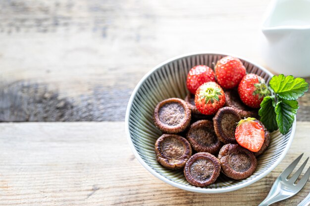 Panqueques de cereales de chocolate en un tazón con fresas y crema