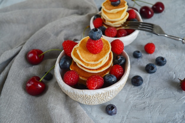 Foto panqueques de cereales, mini panqueques en un bol con arándanos, frambuesas, cerezas. nutrición saludable. tendencia culinaria. comida hecha en casa.