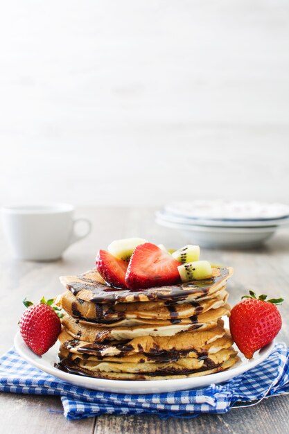 Panqueques con chocolate, fresas y kiwi en mesa de madera