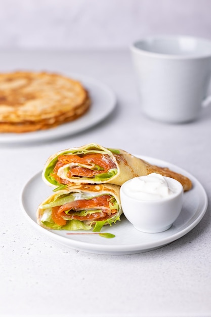 Panqueques con crema agria de trucha de salmón y cosas verdes Blinchiki fino no dulce relleno de pescado rojo Plato tradicional ruso y ucraniano Fiesta de Maslenitsa Primer plano de enfoque selectivo