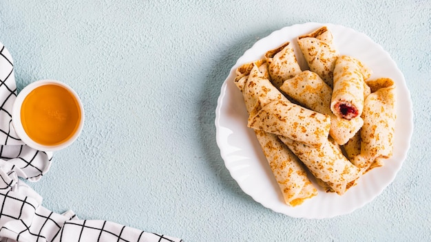 Panqueques delgados enrollados en rollos con mermelada de bayas en un plato en la mesa