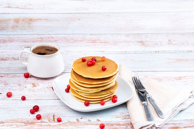 Panqueques de desayuno por la mañana con arándanos en una mesa de madera y una taza de café.
