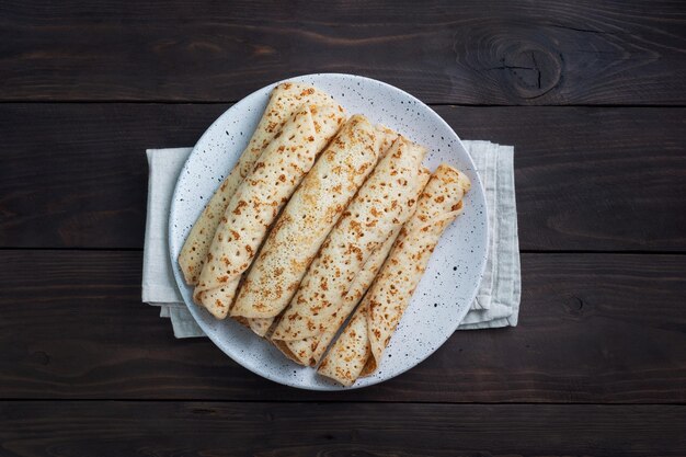 Panqueques finos enrollados en un rollo en un plato El concepto de un delicioso desayuno o espacio de copia de fondo de madera Maslenitsa