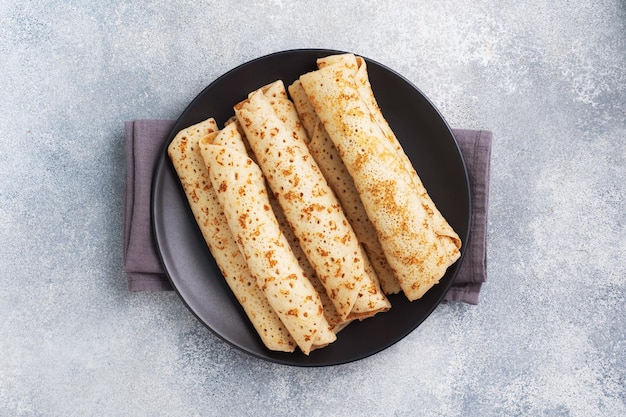 Panqueques finos enrollados en un rollo en un plato El concepto de un delicioso desayuno o fondo de hormigón Maslenitsa