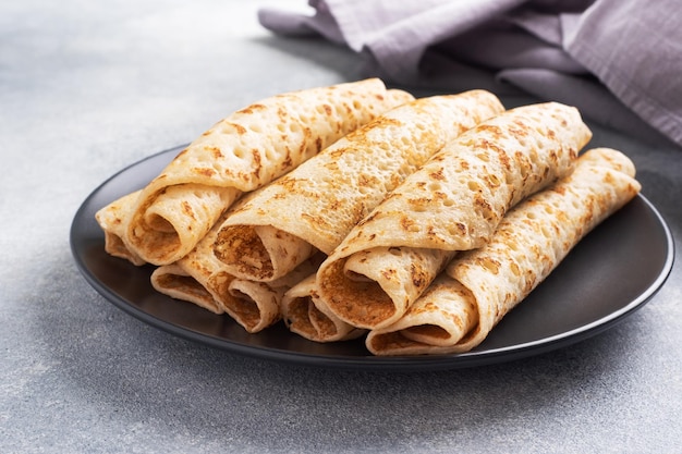 Panqueques finos enrollados en un rollo en un plato El concepto de un delicioso desayuno o fondo de hormigón Maslenitsa