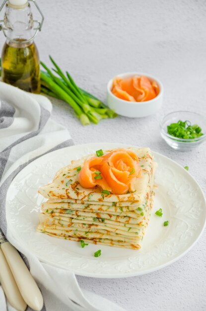 Panqueques finos o crepes rusos tradicionales con queso, hierbas y salmón ahumado en un plato blanco sobre una superficie ligera Vacaciones maslenitsa. Orientación vertical