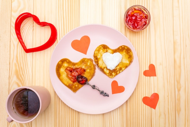 Foto panqueques en forma de corazón para un desayuno romántico con mermelada de fresa y té negro