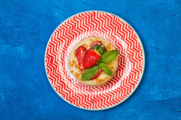 Panqueques con fresas en un plato rojo y blanco y sobre un fondo azul clásico