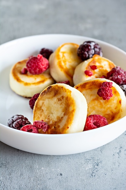 Panqueques frescos de requesón o ricotta syrnikifritters en un plato blanco con bayas frescas sobre un fondo azul Delicioso desayuno saludable Cocina rusa ucraniana comida dulce