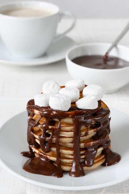 Panqueques con jarabe de chocolate y taza de café en mesa blanca