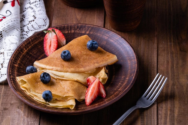 Panqueques con jarra de fresas y arándanos con platos de cerámica de leche al estilo rústico