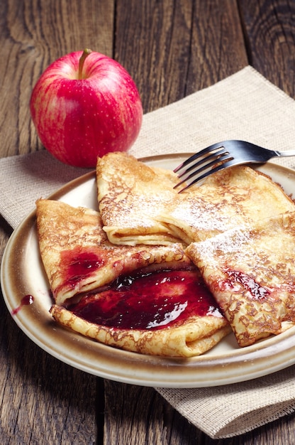 Panqueques con mermelada y manzana roja sobre fondo de madera vintage