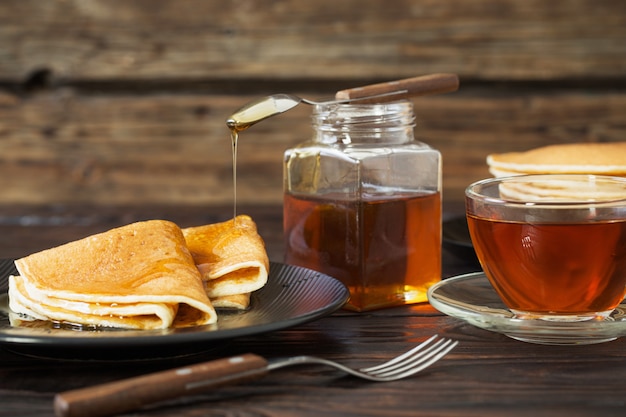 Panqueques con miel y una taza de té en la mesa de madera vieja