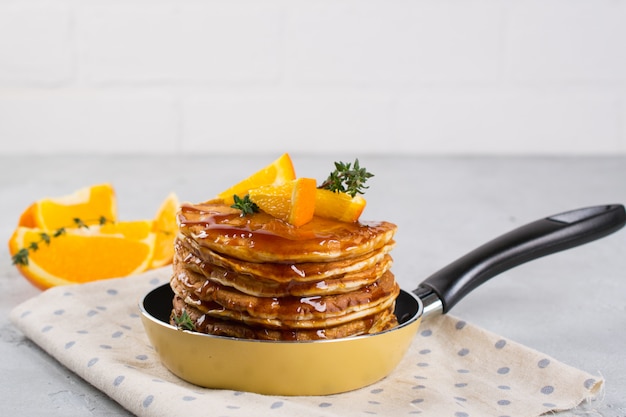 Foto panqueques con naranja y jarabe de arce espolvoreado en una sartén amarilla pequeña sobre superficie blanca. desayuno
