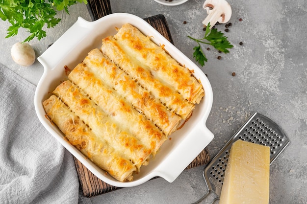 Panqueques o crepes finos rellenos de pollo y champiñones al horno con queso en una fuente para horno