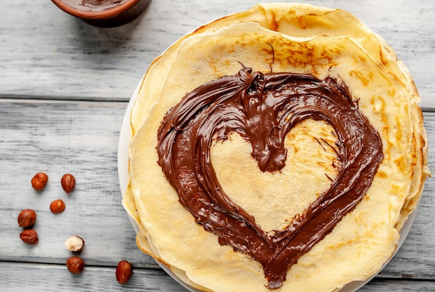 Panqueques con pasta de chocolate y avellanas, corazón dibujado en panqueques en un plato blanco sobre un fondo de madera
