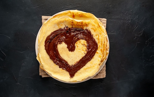 Panqueques con pasta de chocolate y avellanas, se dibuja un corazón en panqueques en un plato blanco sobre un fondo de piedra