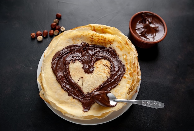 Panqueques con pasta de chocolate y avellanas, se dibuja un corazón en panqueques en un plato blanco sobre un fondo de piedra