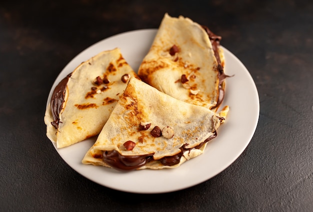 Panqueques con pasta de chocolate y avellanas, en un plato blanco sobre un fondo de hormigón, pizarra