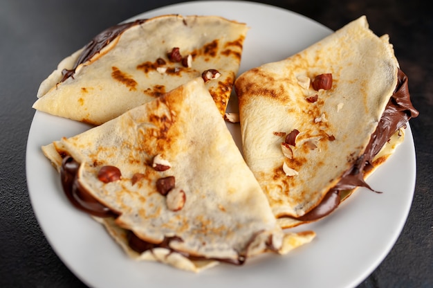 Panqueques con pasta de chocolate y avellanas, en un plato blanco sobre un fondo de hormigón, pizarra